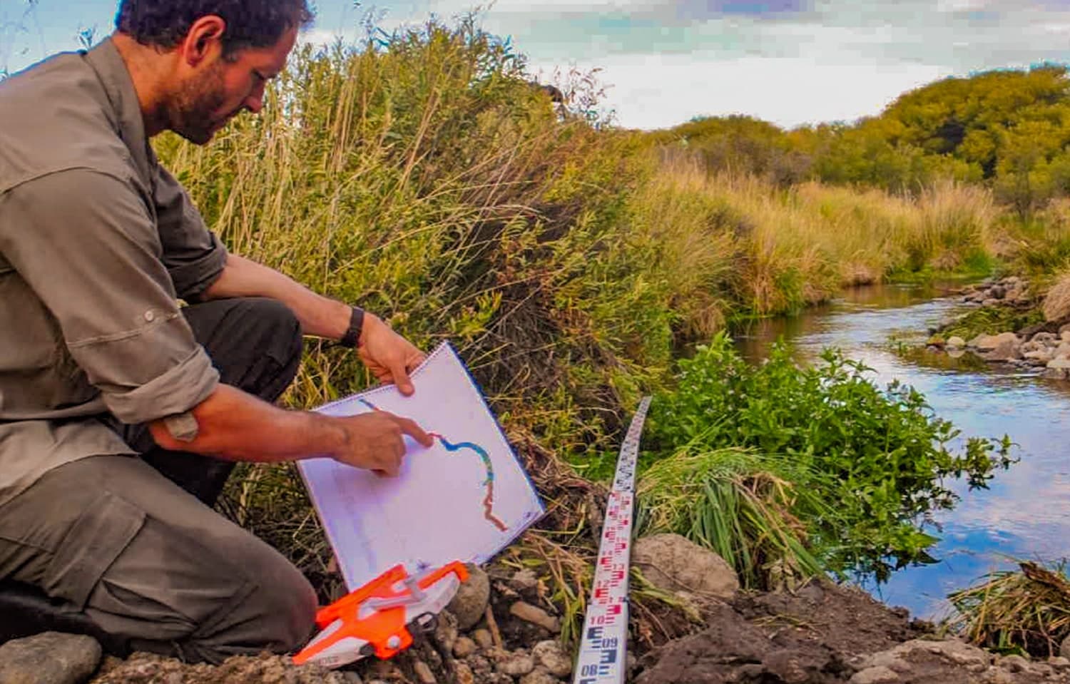 Un técnico señala sobre un plano el trazado del arroyo, sentado en la orilla