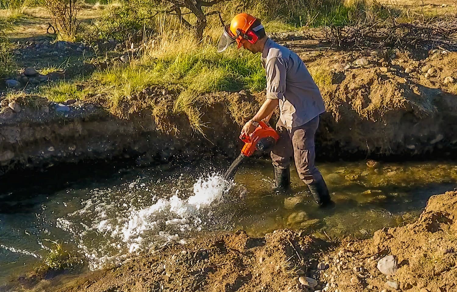 Técnico con casco trabajando sobre el lecho de un arroyo con agua a presión