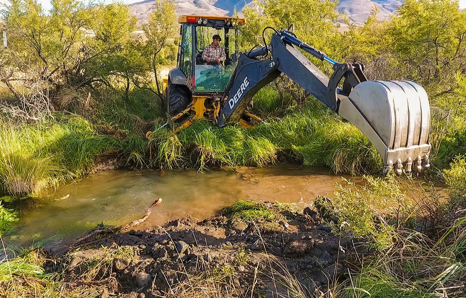 Retroexcavadora trabajando dentro del cauce de un arroyo entre pastizales